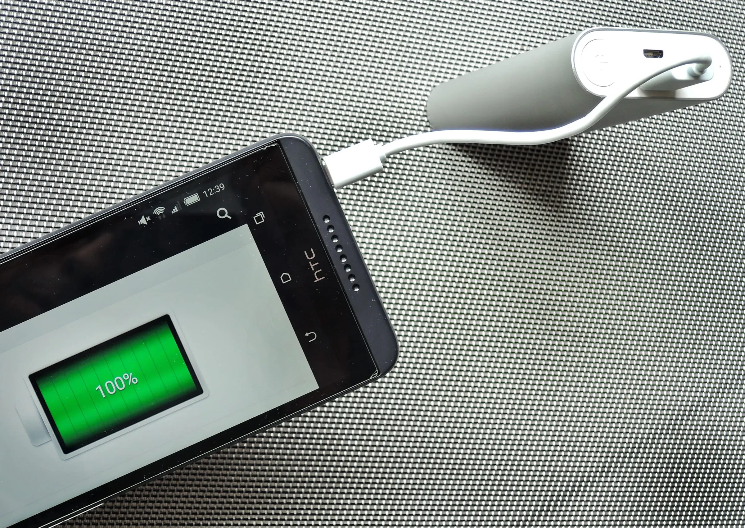 Ein Smartphone wird über ein USB-Kabel von einer kompakten Powerbank mit 10 000 mAh geladen